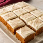Pumpkin Bars topped with a smooth layer of cream cheese frosting and lightly dusted with cinnamon.